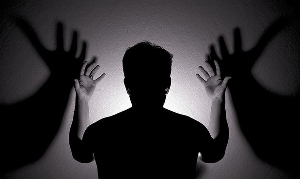 man raising his hands as shadows on the wall